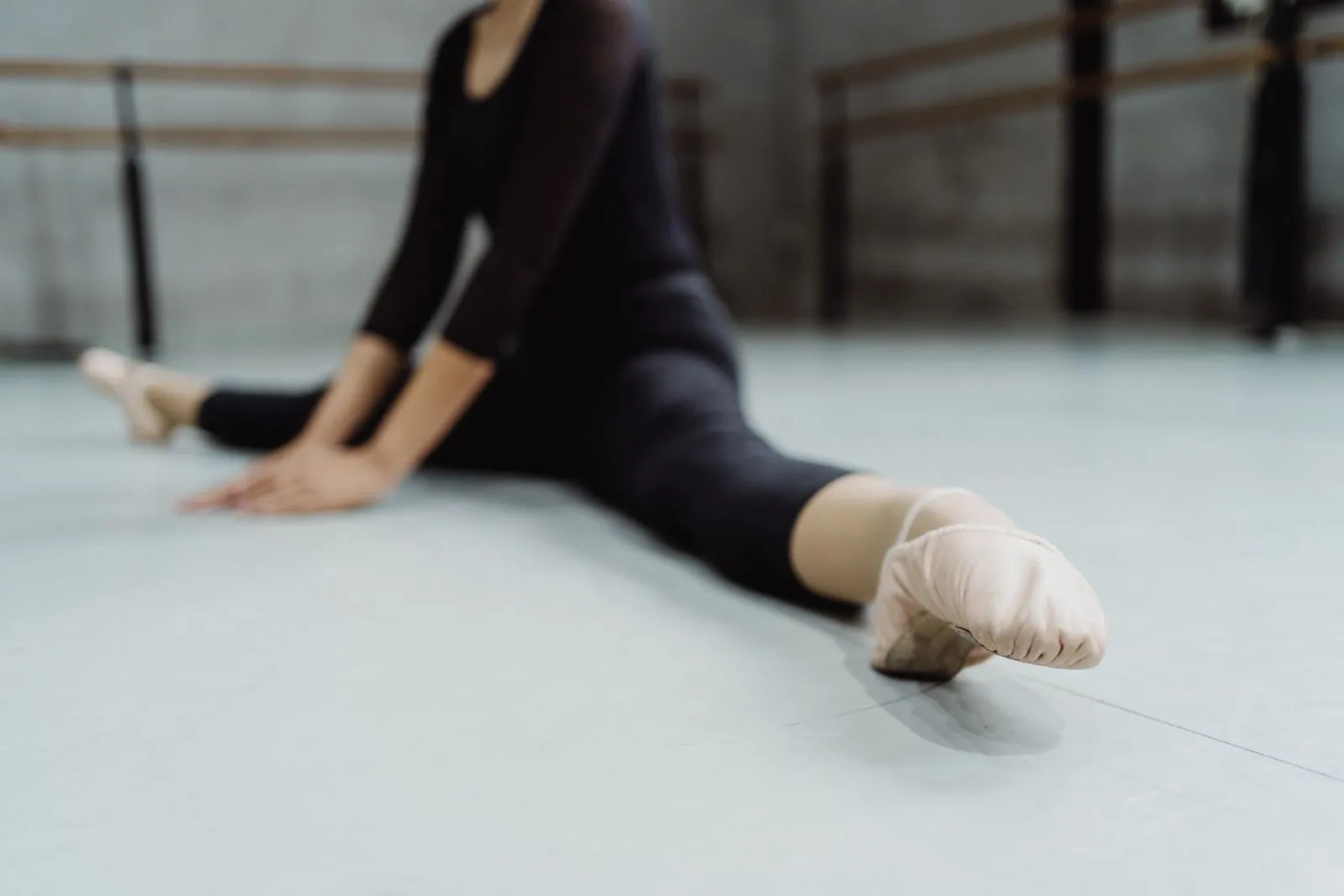 Faceless ballerina warming up during dance rehearsal and stretching muscles of legs in ballet hall